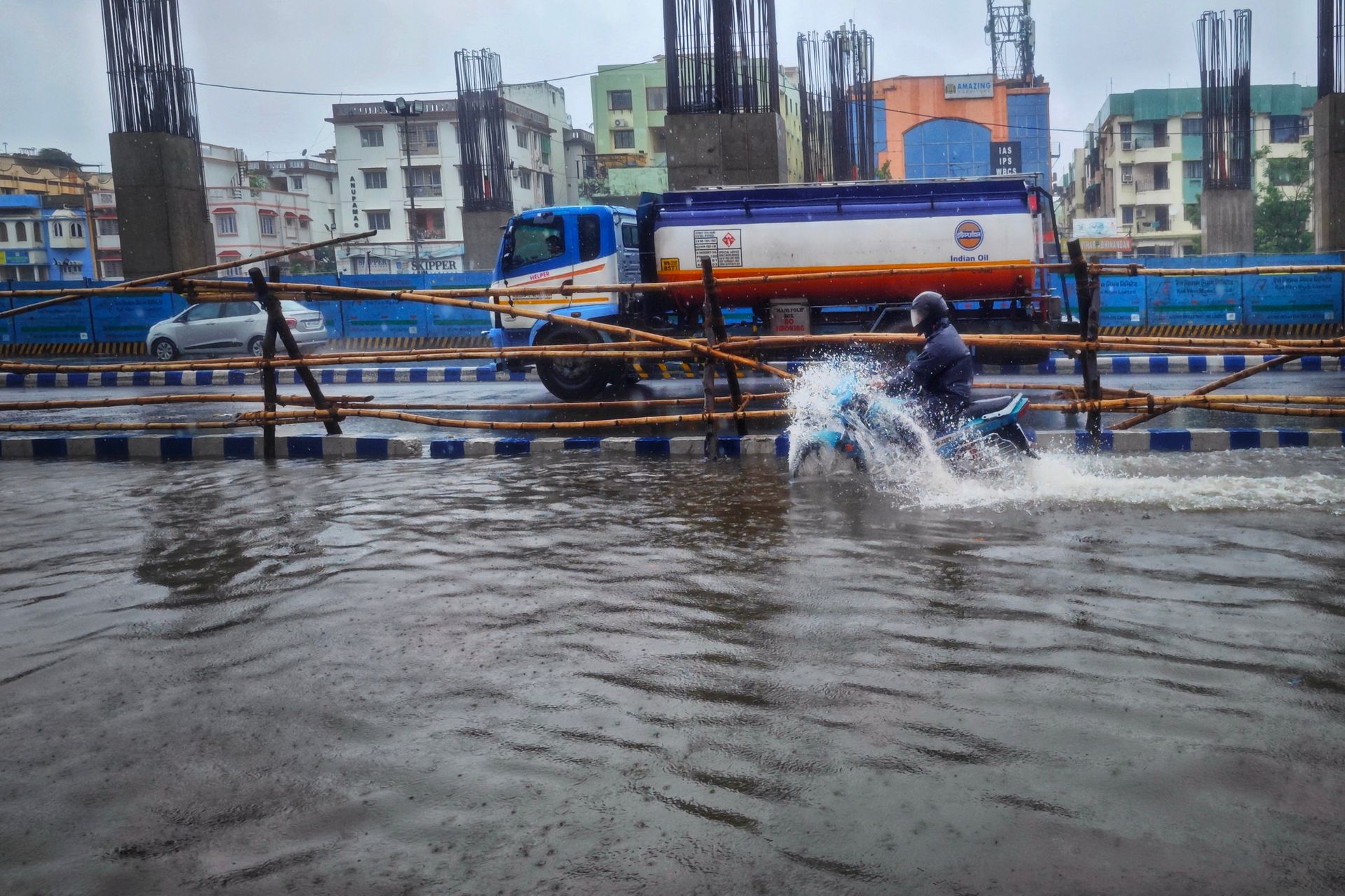 Motorcyclist riding through a flooded street in Kolkata, India during overcast weather.