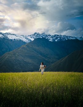 A woman strolls through a field with majestic snow-capped mountains in Maras, Perú.