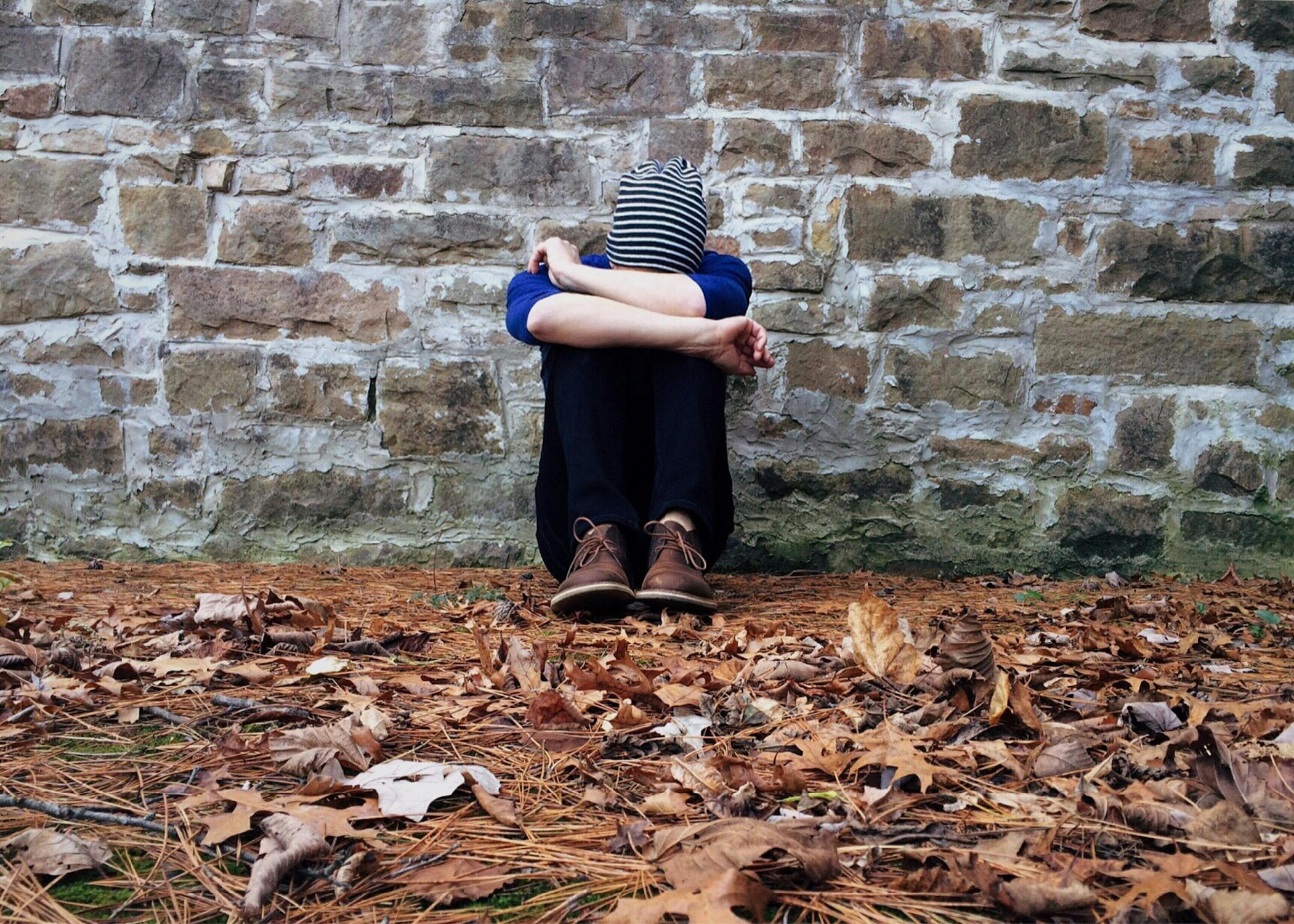 person sitting against wall with head down between legs.