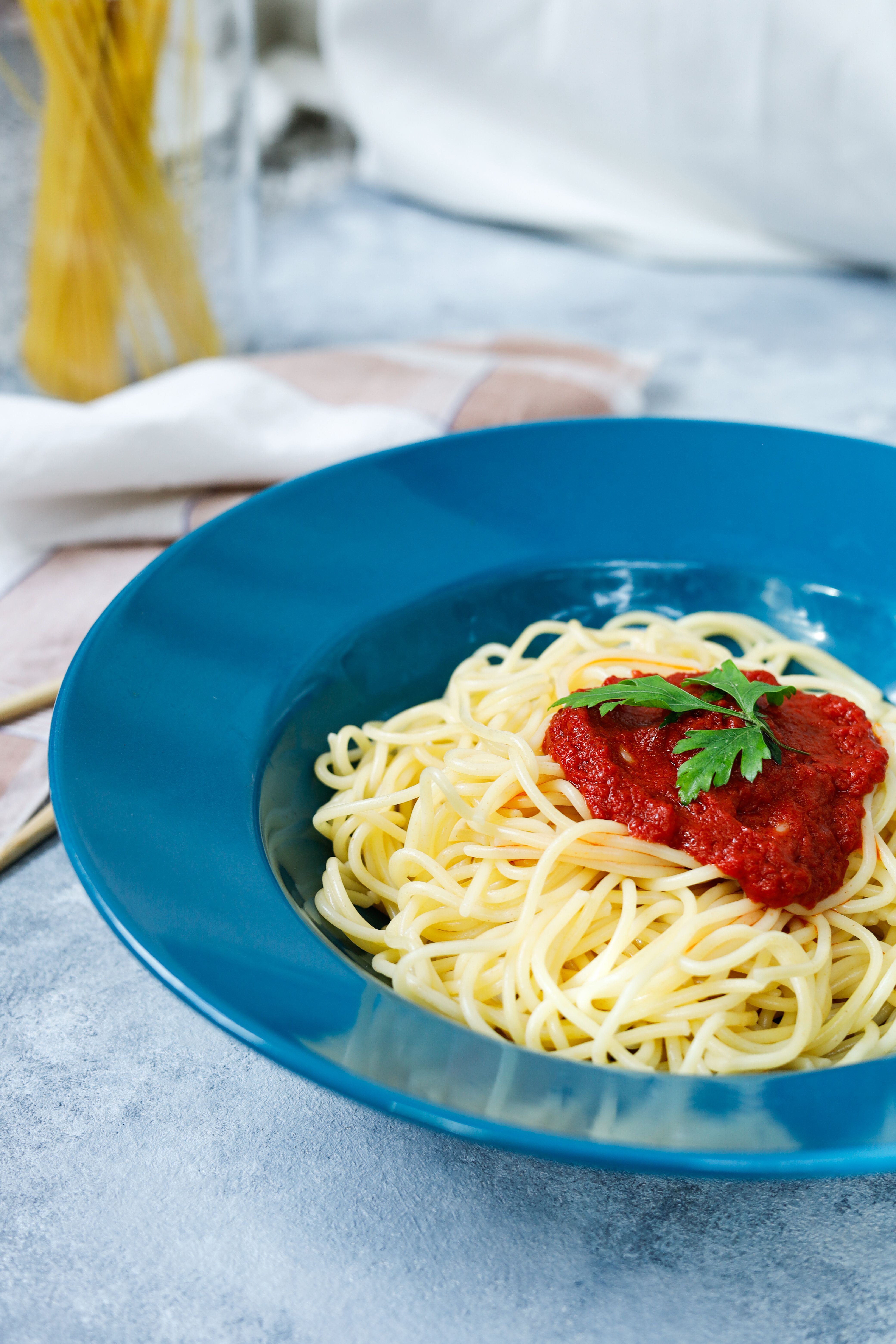 Appetizing spaghetti topped with tomato sauce and parsley in vibrant blue dish, perfect for Italian cuisine lovers.