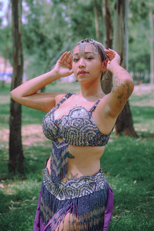 Free Young woman in a sparkling costume poses confidently in a park setting during summer. Stock Photo