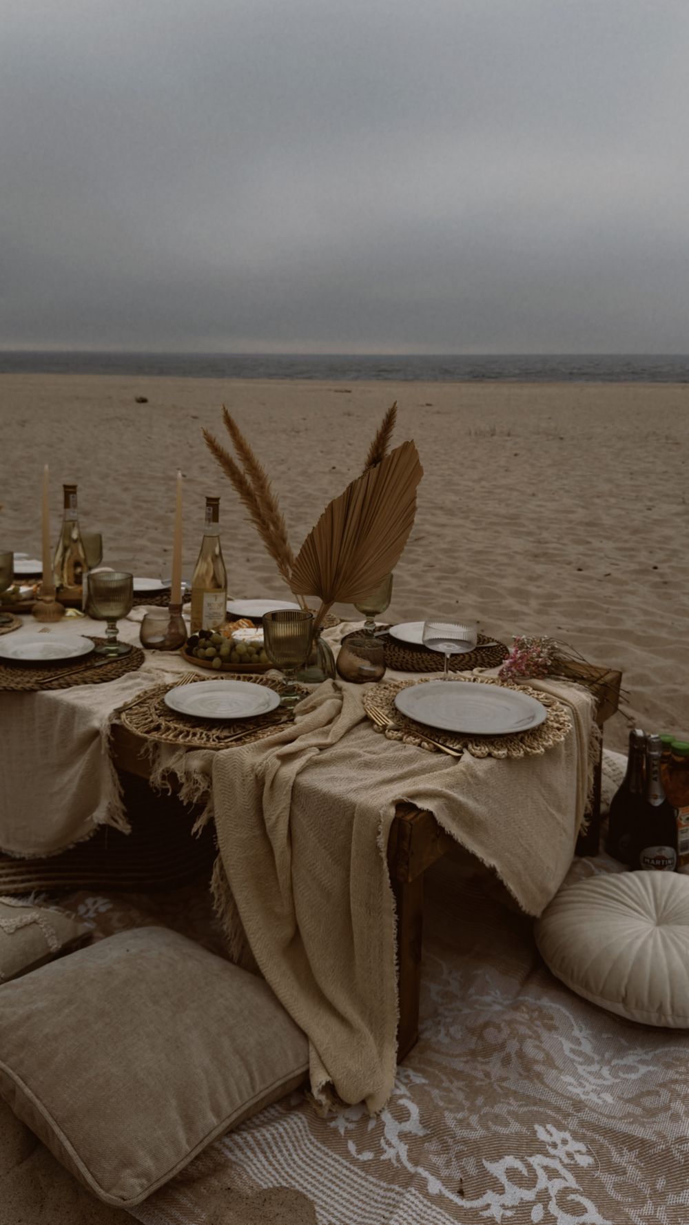 A dressed table on the beach at dusk with candles, dried pampas and every place set