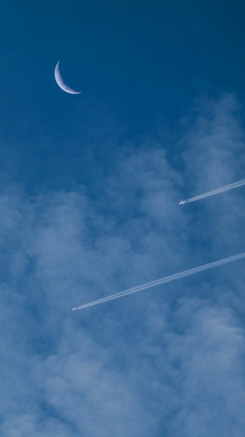 A plane flying through the sky with a crescent moon