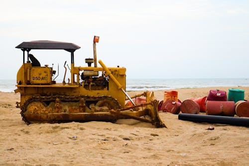 a bulldoser escavator in  the sea shore a rusted bulldoser  with some oil barrels around it