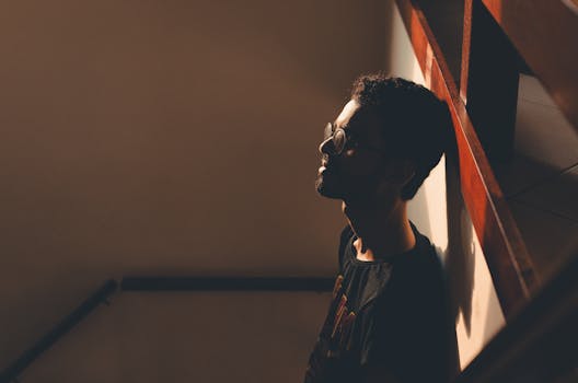 从上方看，一个戴眼镜、留着胡子的年轻男子靠在家里的墙上