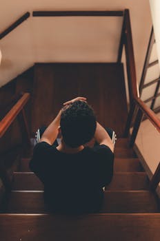从上面看，一名男子若有所思地坐在室内的木楼梯上