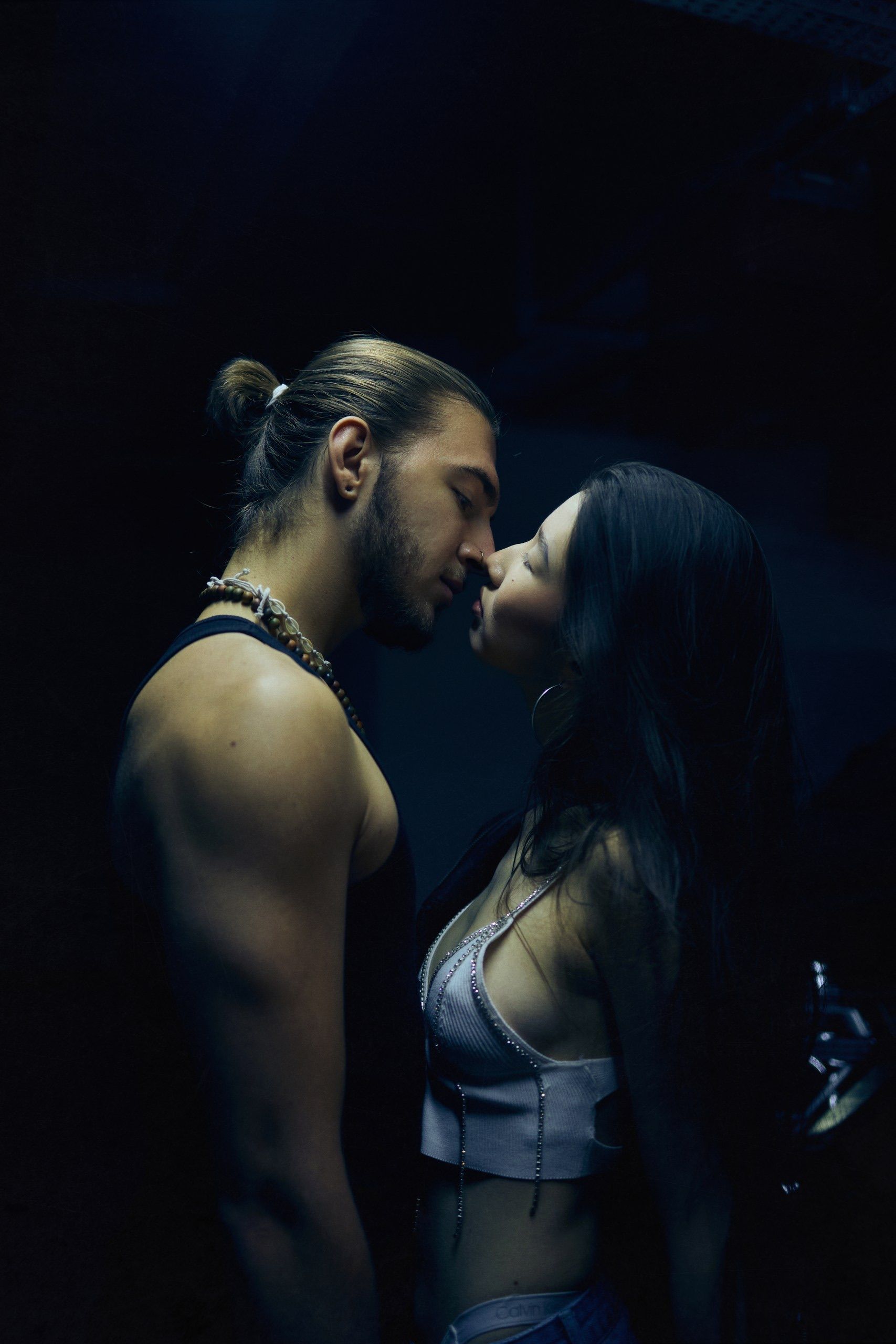 A romantic moment captured of a couple embracing and kissing in a dark, atmospheric setting.