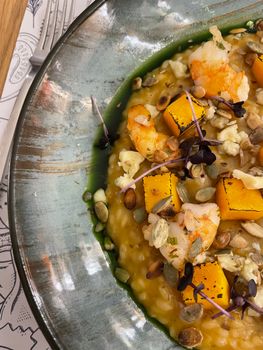Close-up of pumpkin shrimp risotto garnished with seeds on a plate.