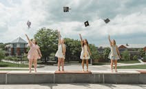 四名女毕业生在户外仪式上高兴地抛起帽子，庆祝学业成功