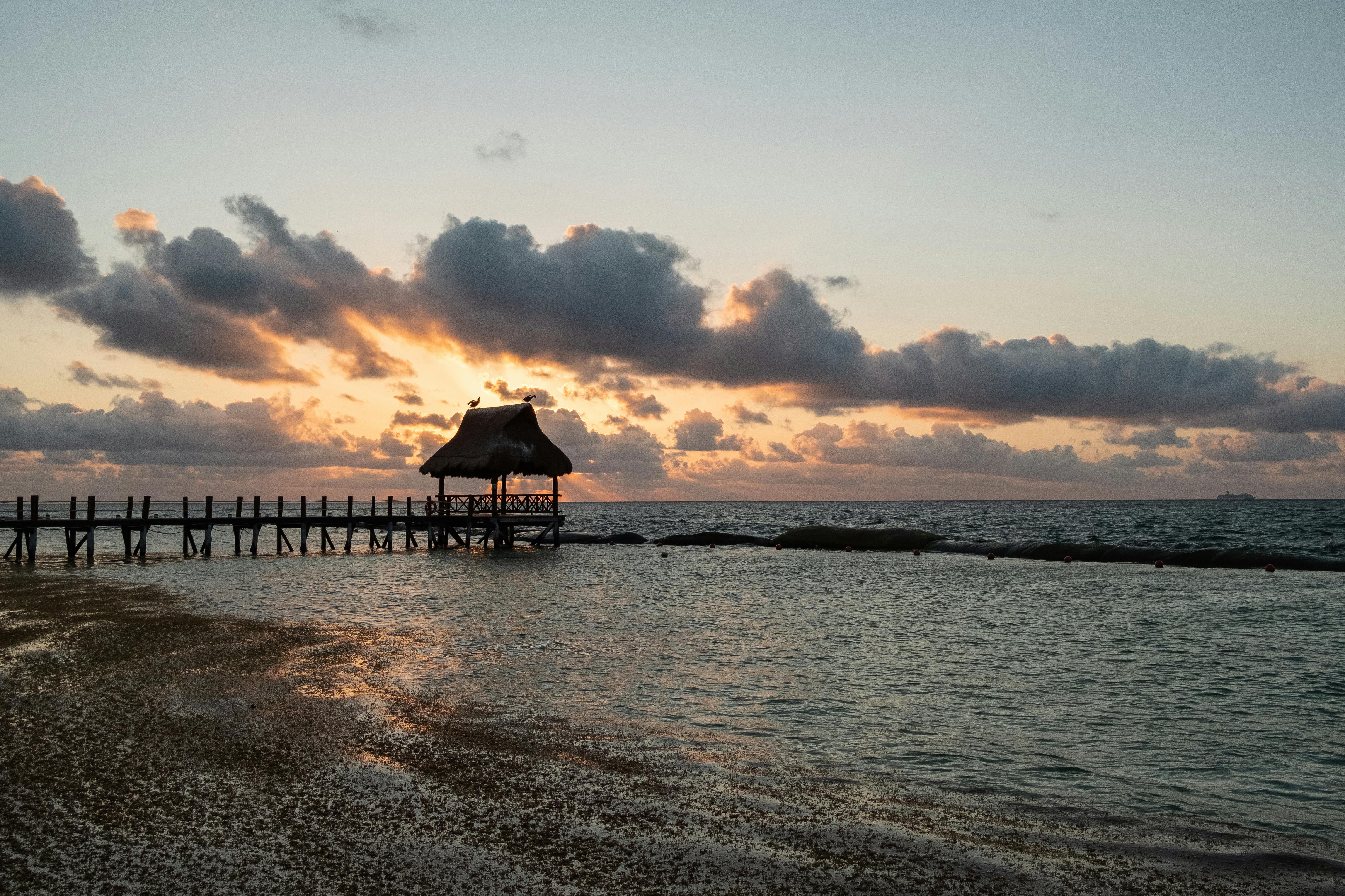 Captivating sunrise at Playa del Carmen with a pier extending into the ocean, under dramatic clouds.