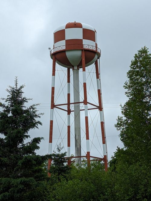Free A striking red and white water tower stands tall amidst lush greenery under an overcast sky. Stock Photo