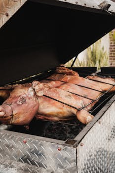 A close-up shot of a whole pig being roasted on a metal barbecue grill outdoors.
