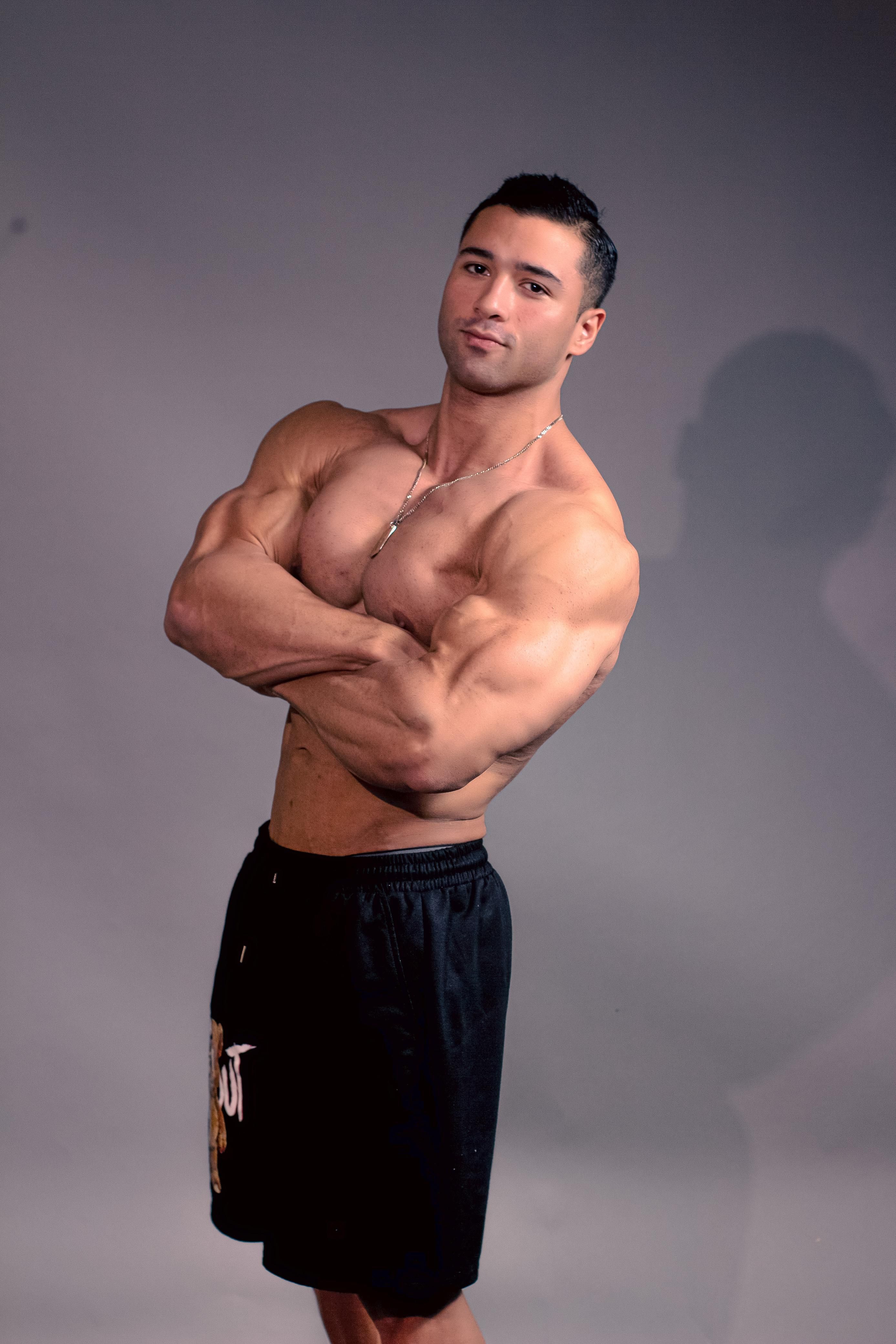 Muscular topless sportsman posing confidently in studio setting with arms crossed.