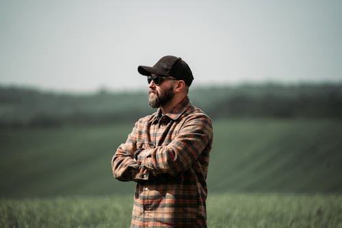 Free A man in a plaid shirt and hat stands in a field Stock Photo