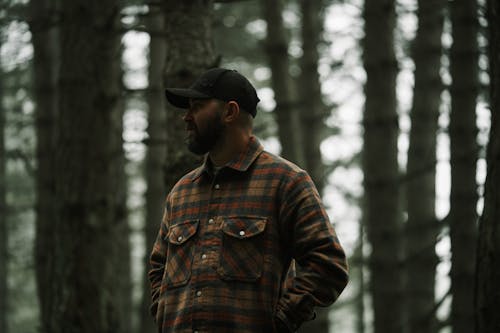 A man in a plaid shirt stands in the woods