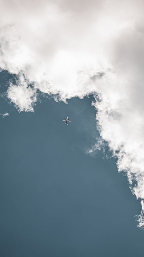 Free Aerial view of an airplane soaring amidst dramatic, fluffy clouds in a clear blue sky. Stock Photo