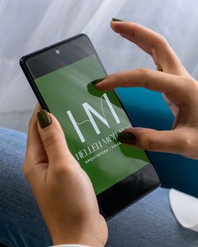 Female hands holding smartphone displaying 'Hellet Morais' logo, close-up.