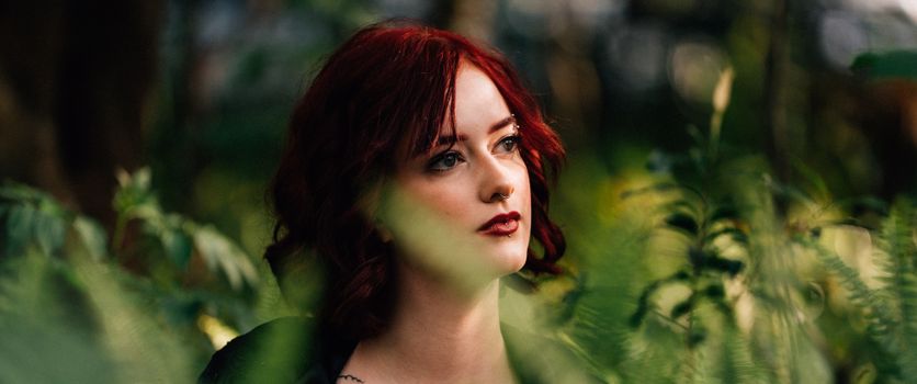Portrait of a redhead woman surrounded by ferns, with a dramatic and moody atmosphere.