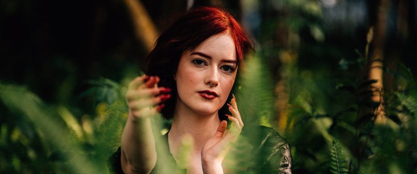 Striking portrait of a woman amidst lush fern foliage, bathed in natural light.