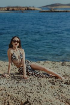 Woman in leopard print bikini relaxing on rocky sea shore. Sunny summer day.