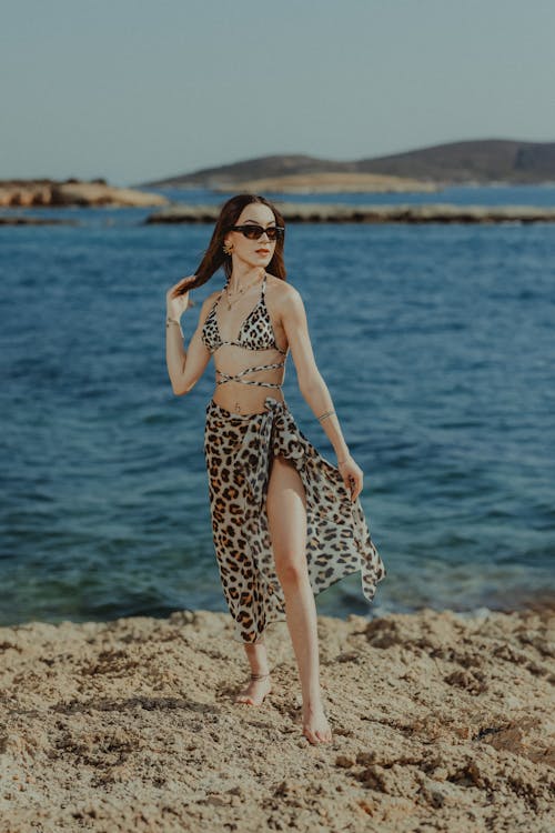 A woman in a leopard print dress and sunglasses standing on the beach