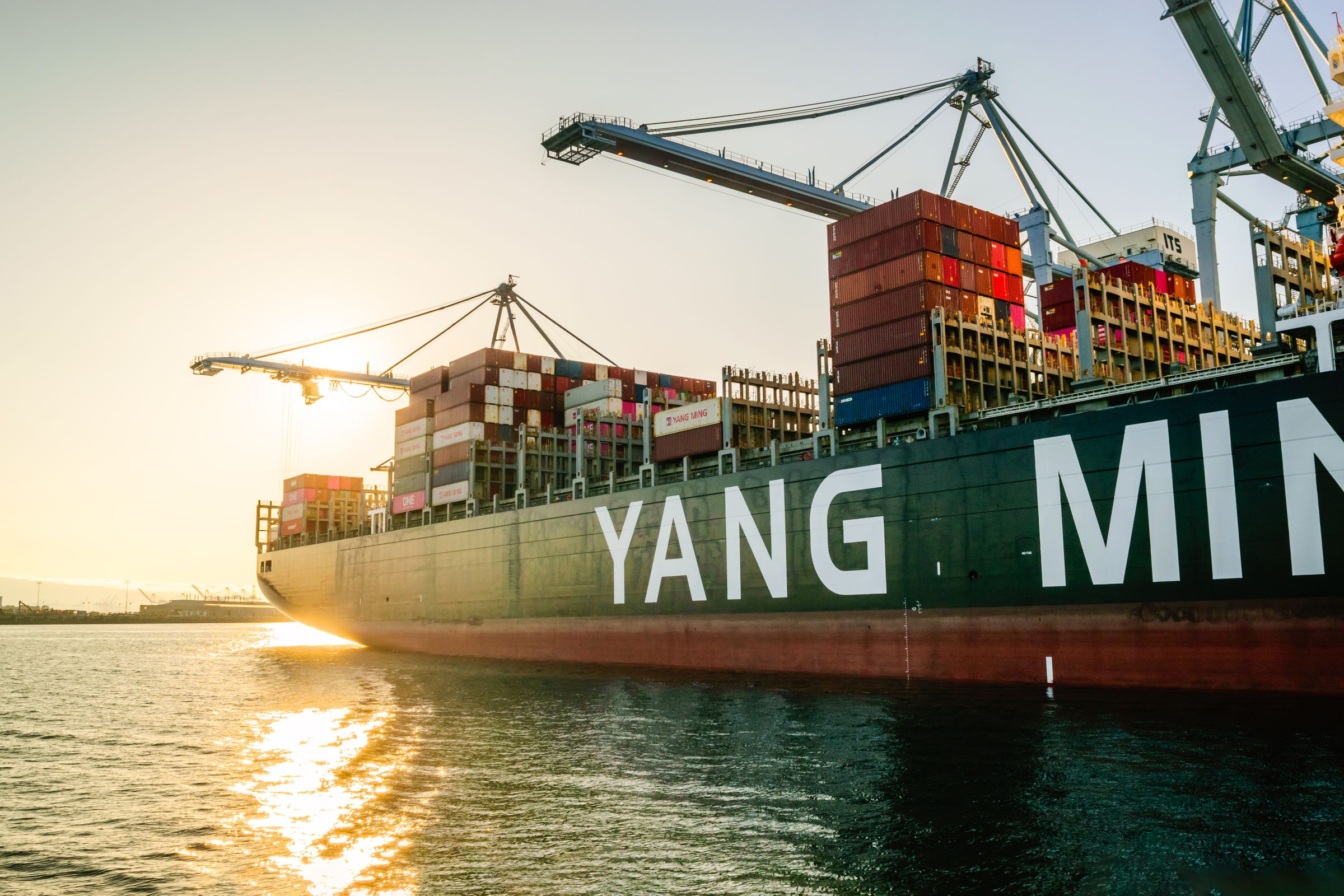 Container ship in harbor at sunset with port cranes
