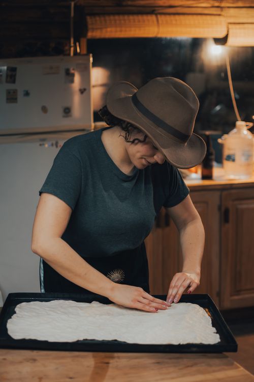 Free A woman in a hat shapes dough on a tray in a cozy kitchen environment, showcasing home baking. Stock Photo