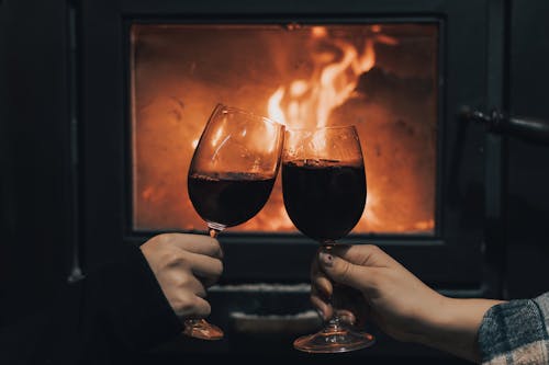 Two people holding glasses of wine in front of a fireplace