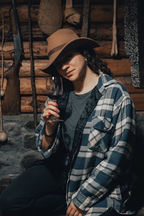 A woman in a hat and plaid shirt holding a wine glass