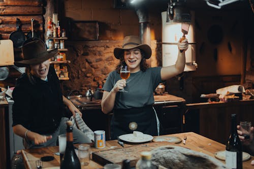 Two women in hats and aprons are holding up glasses