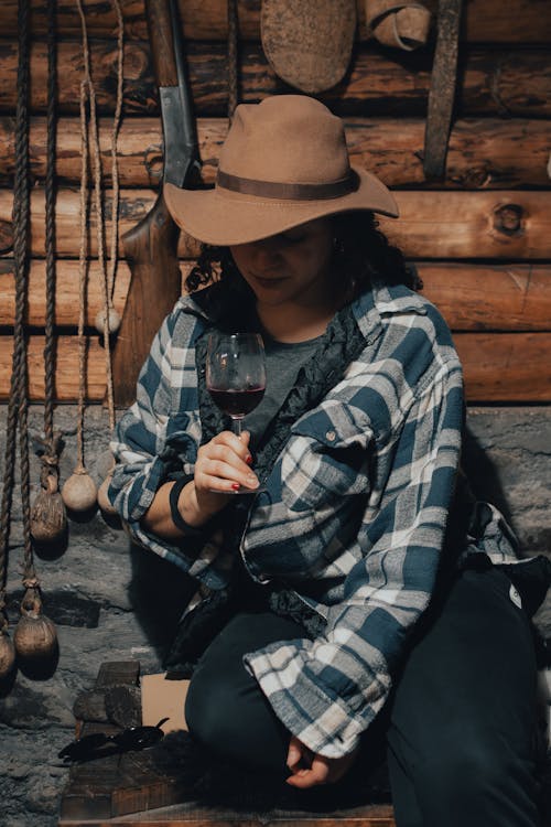 A woman in a hat and plaid shirt is holding a wine glass