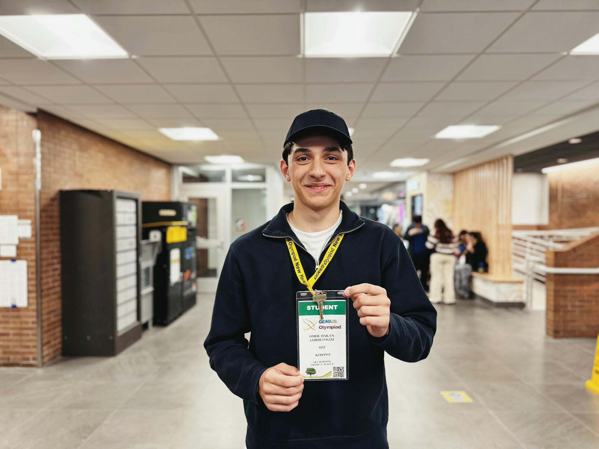 Un jeune étudiant souriant tout en tenant un badge d'identification dans un couloir de l'école, transmettant la convivialité.