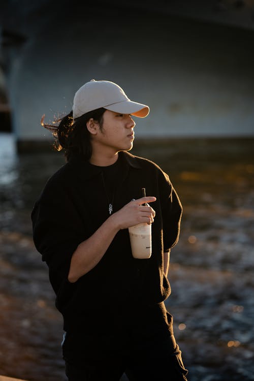 A man in a hat and black jacket holding a drink