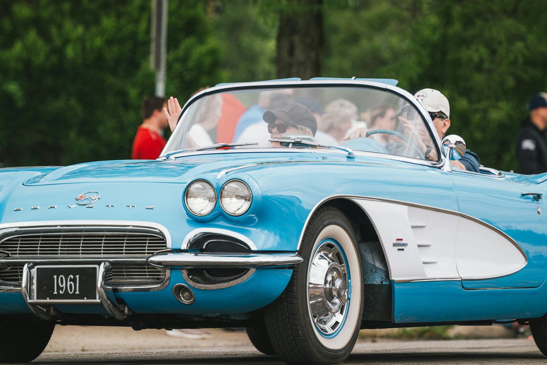 Classic blue 1961 Chevrolet Corvette cabriolet with driver and passenger outdoors.