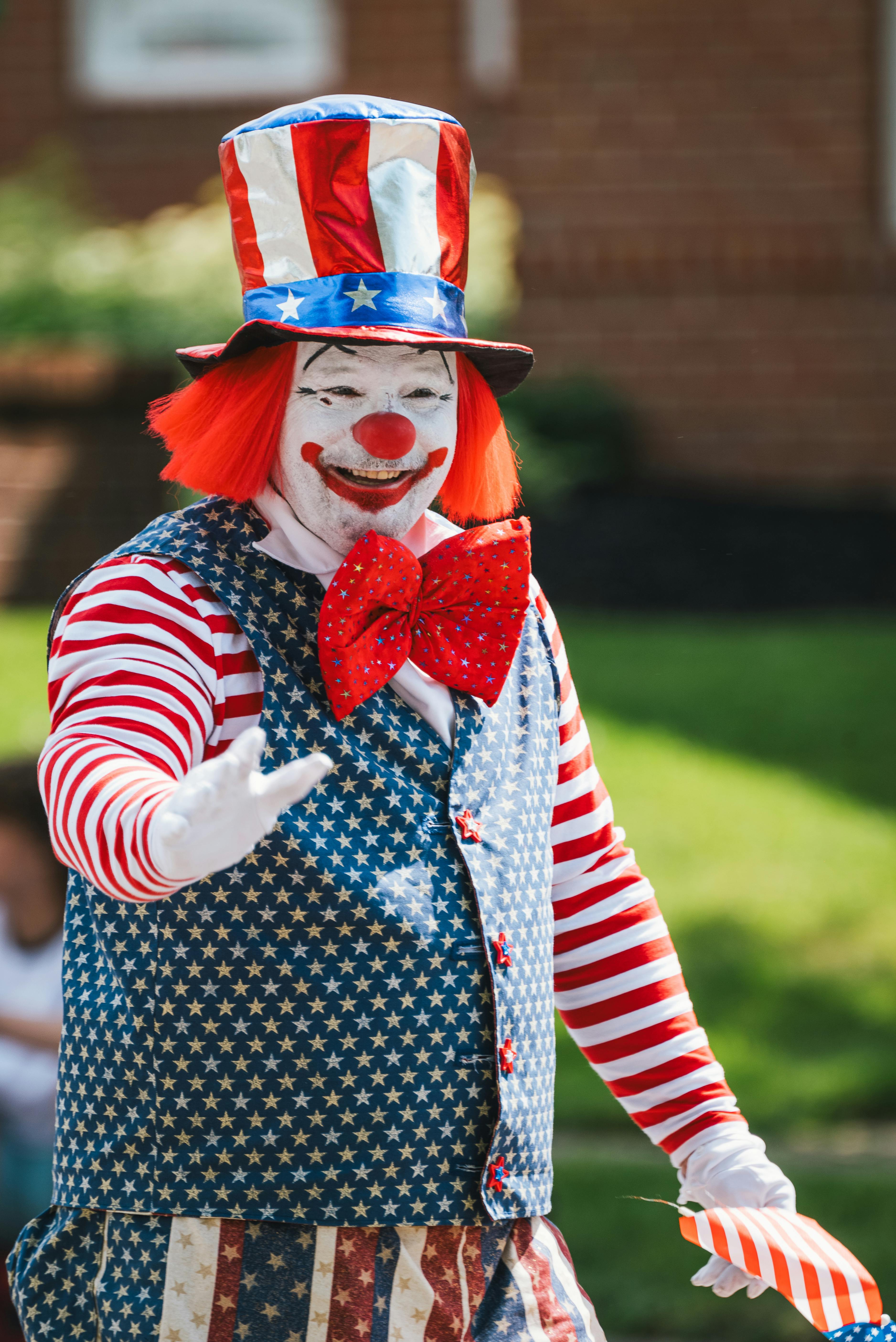 A colorful clown in American themed costume entertains at a sunny outdoor parade.