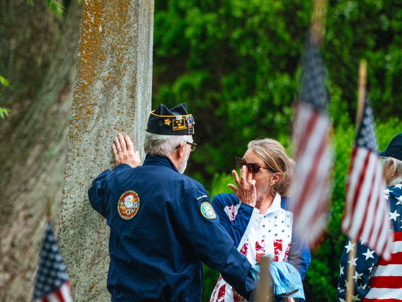 Veterans gathering at a cemetery to honor fallen soldiers during Memorial Day with American flags displayed - veterans group history visits