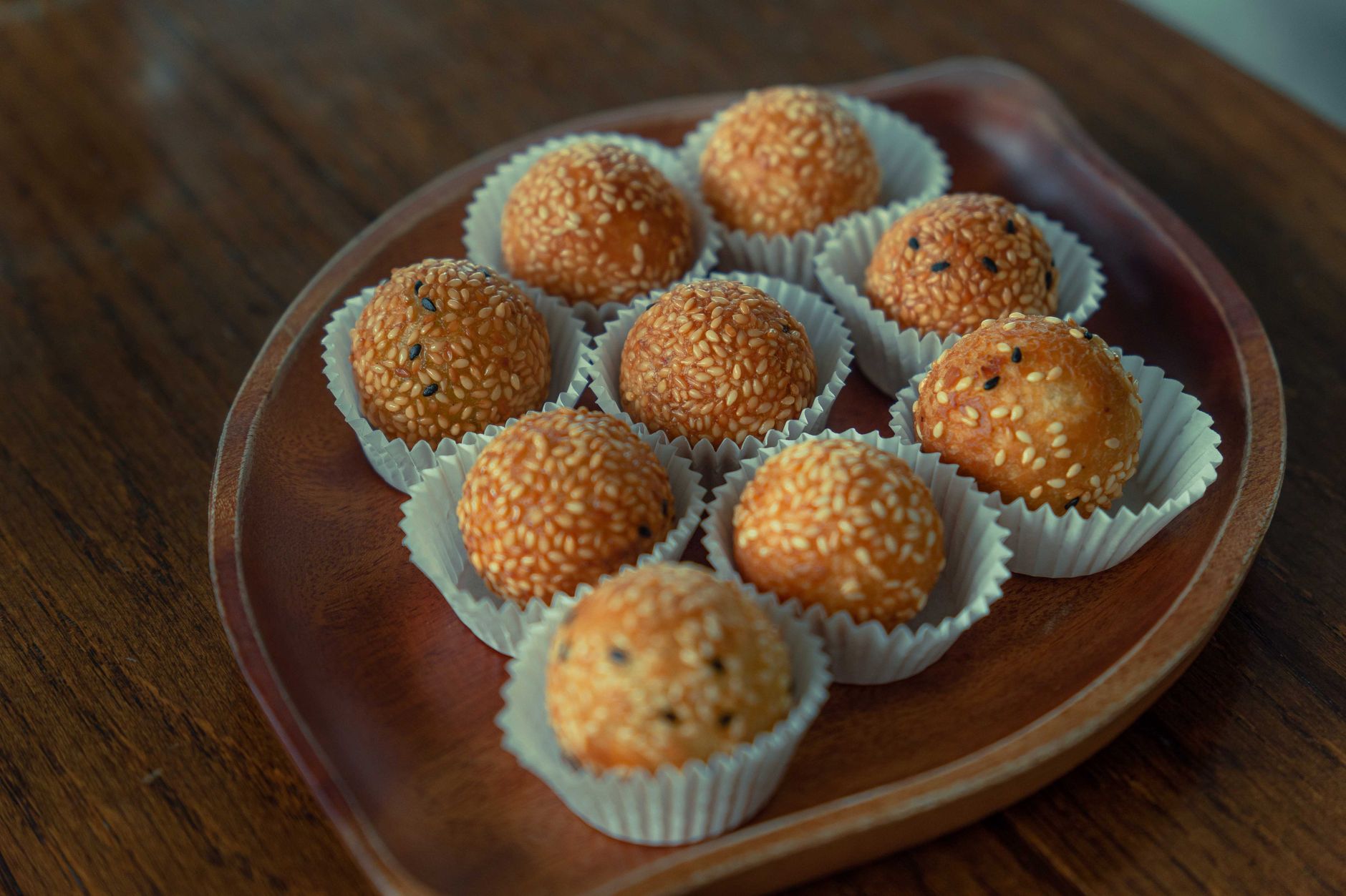 Close-up of delicious Vietnamese sesame banh ran on a wooden plate, showcasing their golden crispy texture.