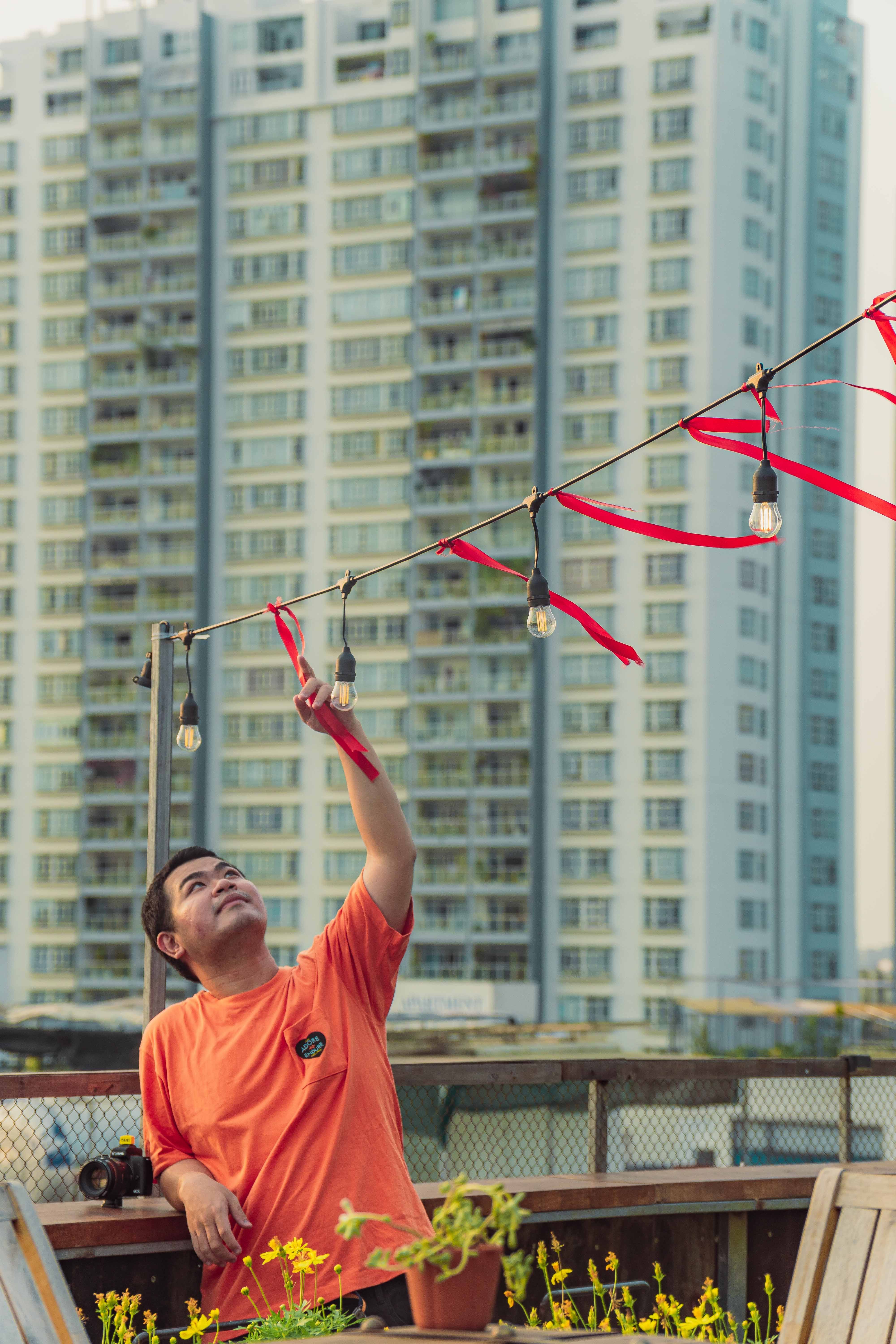 Man adjusts string lights on a rooftop in Ho Chi Minh City, Vietnam with urban high-rise in background.