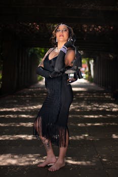 Stylish woman in a black fringe dress poses confidently in an urban tunnel.