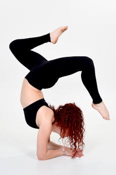Flexible sportswoman performing a handstand in a studio setting on a white background, showcasing athletic strength.