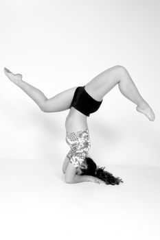 Black and white image of a woman performing a headstand in a studio, highlighting balance and fitness.