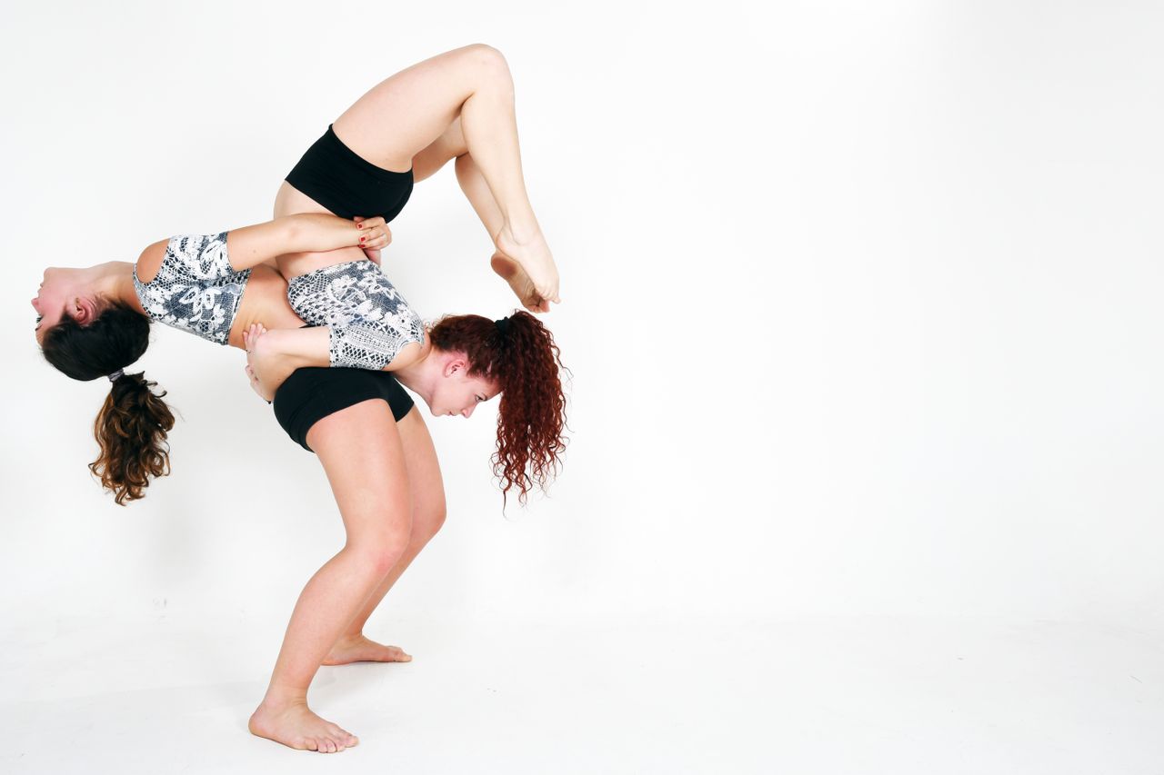 two women performing an acrobatic pose on a white background showcasin