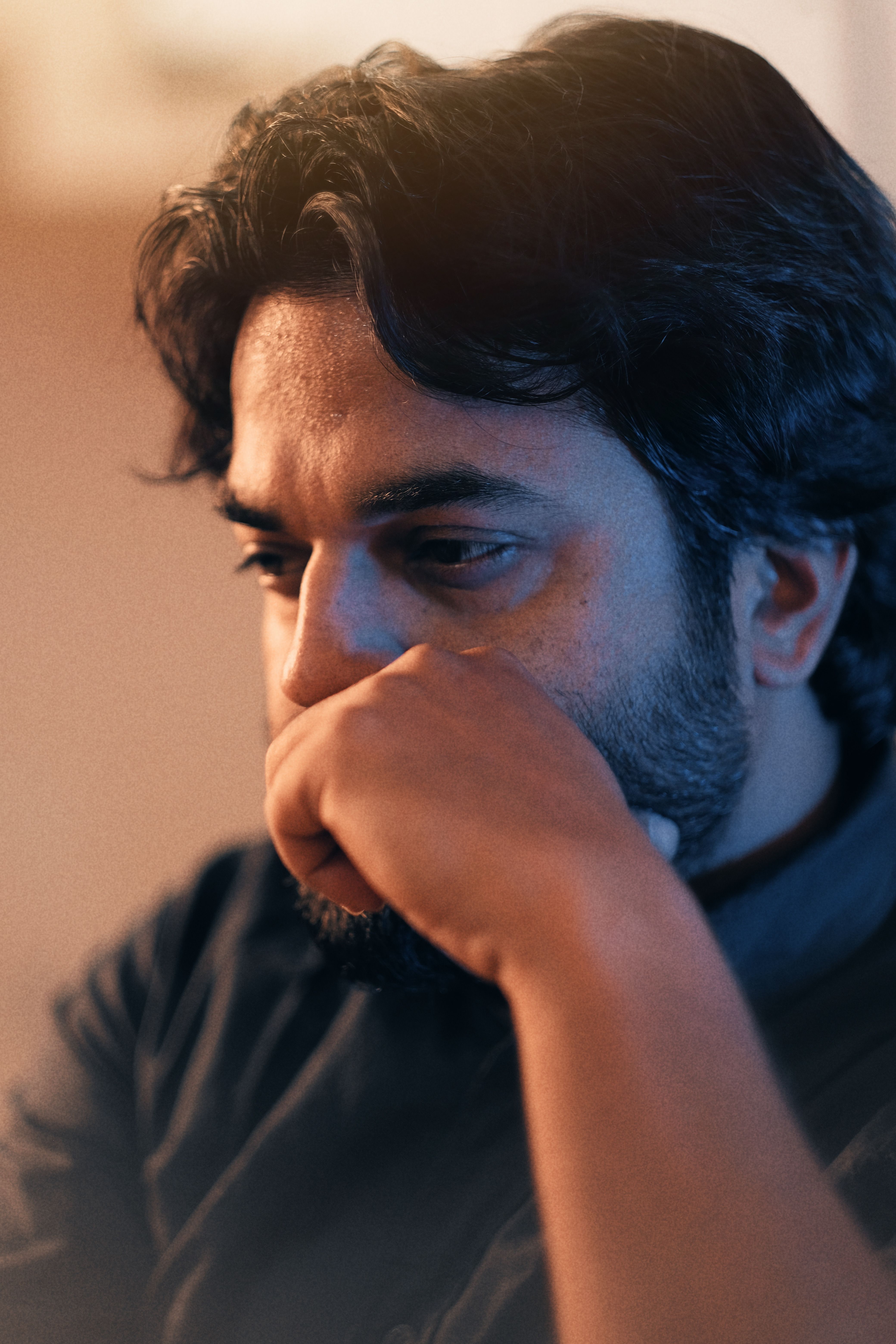 A man with a beard sits pensively, captured in a warm, intimate setting.
