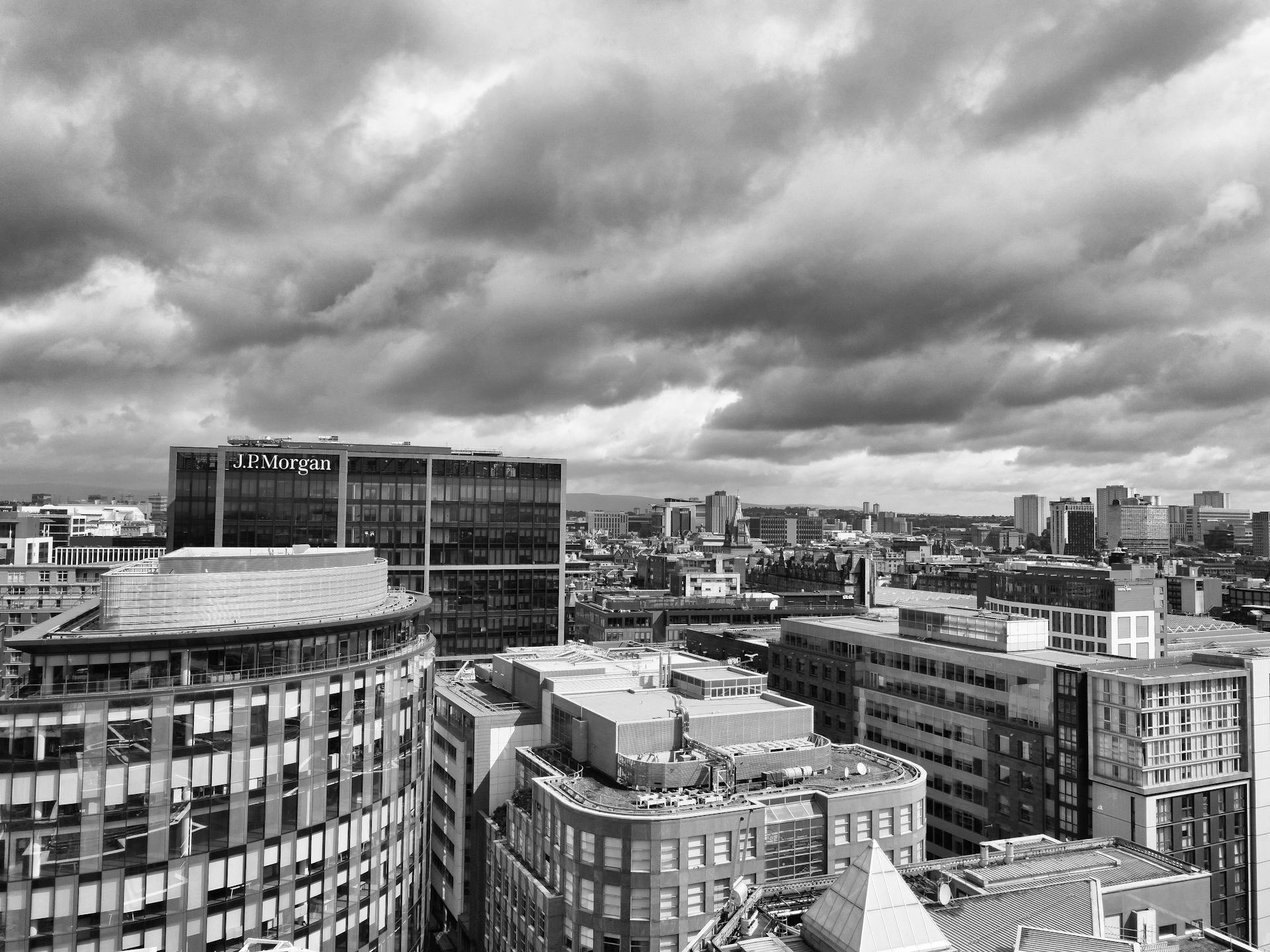 Black and white aerial view of modern Glasgow cityscape under dramatic cloudy skies.