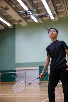 A young boy in sportswear intensely playing badminton inside a gymnasium.