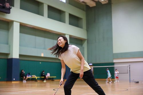 Free Smiling Asian woman playing badminton indoors in a sports hall, wearing casual sportswear. Stock Photo