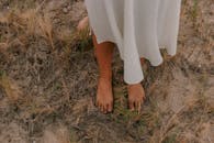 一名白衣女子赤脚站在干燥的沙草地上，营造出异想天开的户外场景