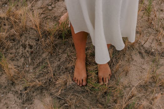 一名白衣女子赤脚站在干燥的沙草地上，营造出异想天开的户外场景