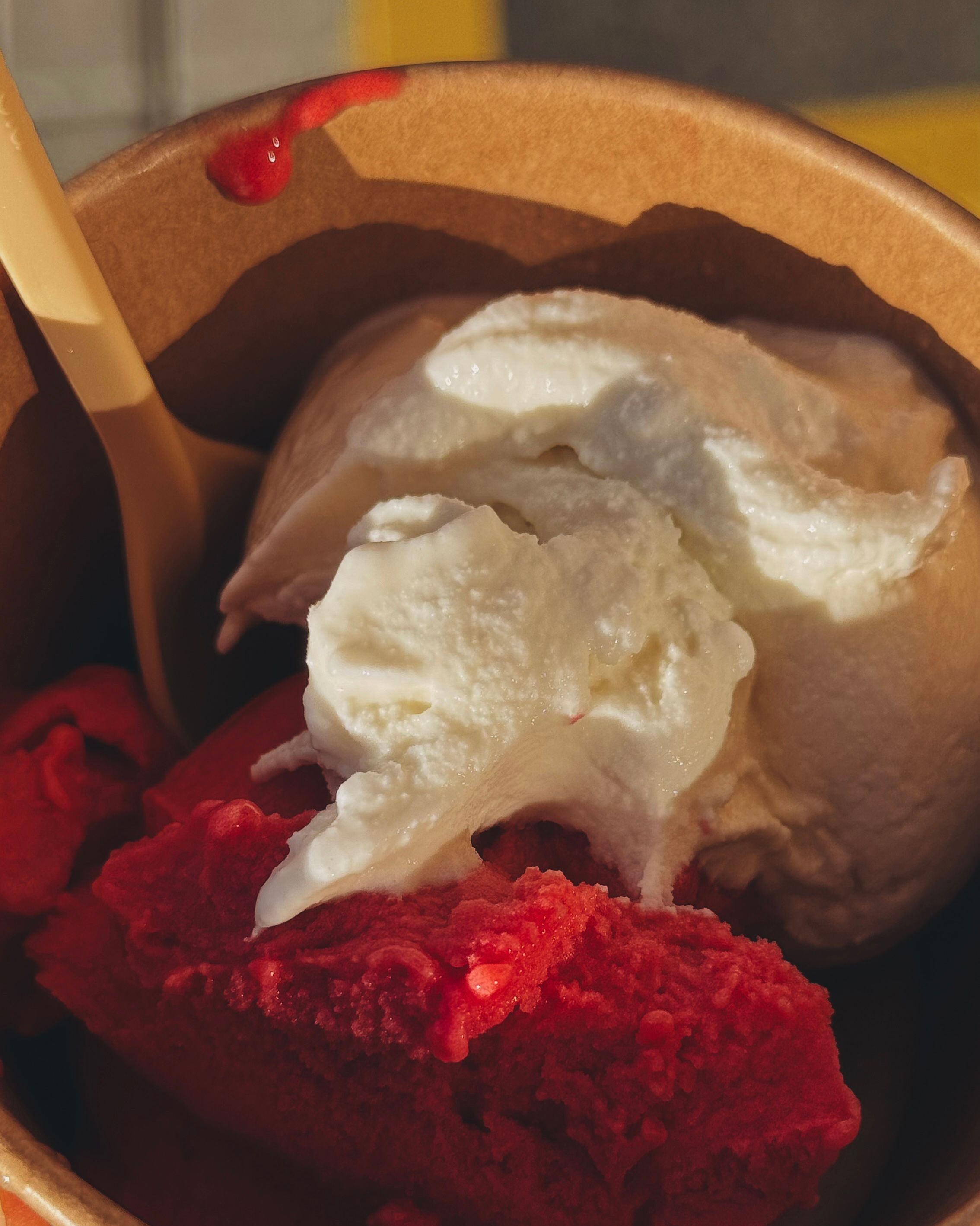 Close-up of vanilla and raspberry gelato scooped in a bowl under warm sunlight.