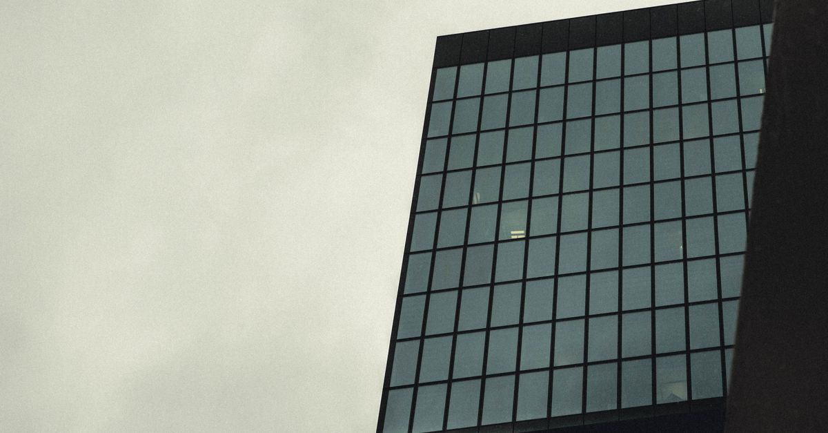 Low angle view of a modern skyscraper with a glass facade against a cloudy sky.